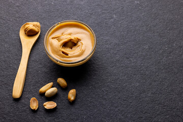 Image of spoon and bowl with peanut butter and nuts on dark grey surface