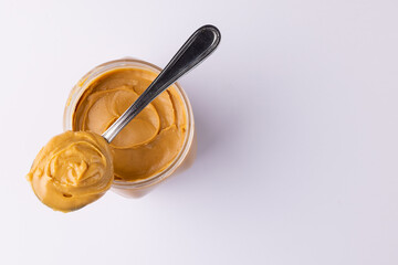 Image of spoon and jar with peanut butter on white surface