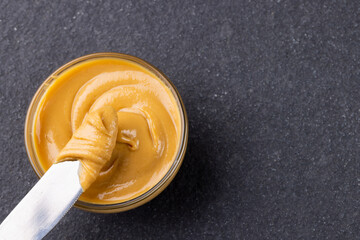 Image of knife and bowl with peanut butter on dark grey background