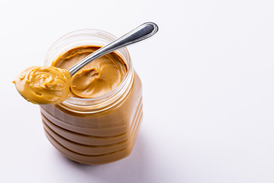 Image of spoon and jar with peanut butter on white surface