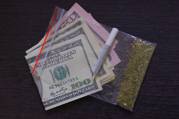Bag of marijuana or weed on dollars. Drug trading concept. Shredded cannabis joint on a brown wood background close up