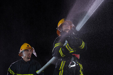 Firefighters using a water hose to eliminate a fire hazard. Team of female and male firemen in dangerous rescue mission. 