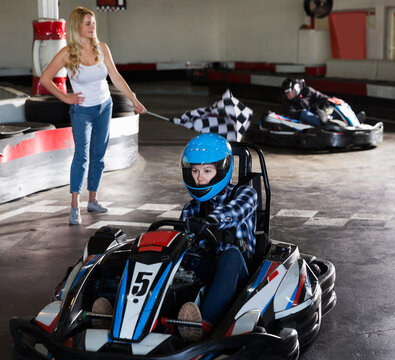 active woman driving sport car for karting in sport club, woman with race flag on background