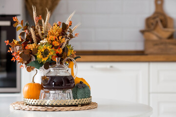 Still-life. Yellow, orange flowers in a vase, pumpkins and a teapot on a golden tray on a white table in the interior of a Scandinavian-style home kitchen. Cozy autumn concept.