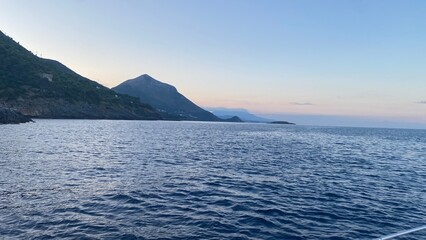 Landscape of the south of Italy from a boat at sunset with high hills, sea till the line of the horizon with past colour in a sunny day