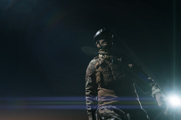 Army soldier in Combat Uniforms with an assault rifle, plate carrier and combat helmet going on a dangerous mission on a rainy night. 