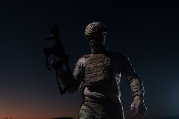 Army soldier in Combat Uniforms with an assault rifle, plate carrier and combat helmet going on a dangerous mission on a rainy night. 
