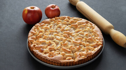 homemade apple pie on a black background in a gray plate with red apples and rolling pin