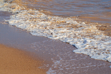 Waves with foam on a sunny summer day on a sandy beach. Nature background. Beach scene with sea waves and sand