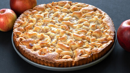 homemade apple pie on a black background in a gray plate with red apples