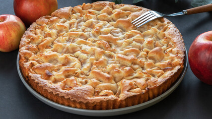 homemade apple pie on a black background in a gray plate with red apples and fork