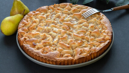 homemade pear pie on a black background in a gray plate with pears and fork