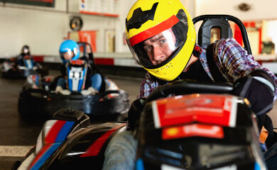 Portrait of happy cheerful positive male racer in helmet driving kart on track