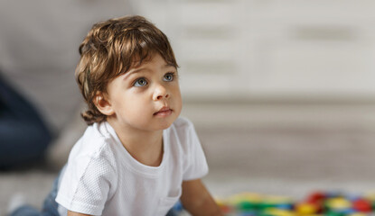 Fototapeta premium A small child looks up sitting on the floor in a room