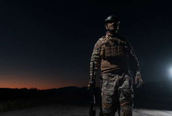 Army soldier in Combat Uniforms with an assault rifle, plate carrier and combat helmet going on a dangerous mission on a rainy night. 