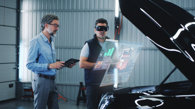 Two specialists carry out car diagnostics using modern tools. They study the indicators and graphs on the screen, displaying the condition of the car. Carrying out repairs in a technological workshop.