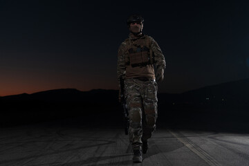 Army soldier in Combat Uniforms with an assault rifle, plate carrier and combat helmet going on a dangerous mission on a rainy night. 