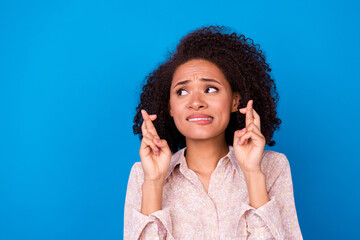 Photo of worried nervous lady bite lips crossed fingers look empty space isolated on blue color background