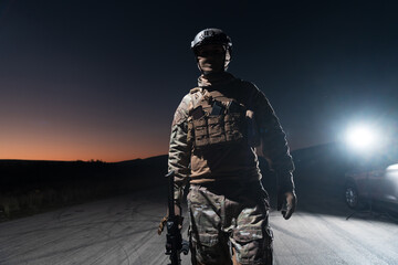 Army soldier in Combat Uniforms with an assault rifle, plate carrier and combat helmet going on a dangerous mission on a rainy night. 