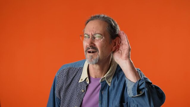 Man struggles to hear, having difficulty hearing, isolated on solid orange background studio portrait.