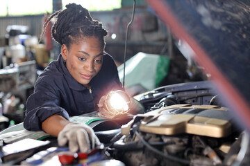 Woman technician car mechanic in uniform checking maintenance car service at repair garage station. Worker holding flashlight and wrench fixing breakdown vehicle. Concept of car center repair service.
