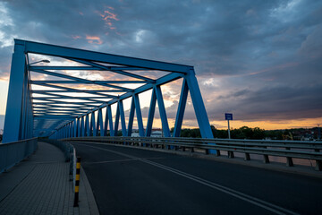 Asphalt road and truss bridge during an evening storm - obrazy, fototapety, plakaty