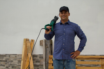 Image of a smiling handyman with a hacksaw on his shoulder while cutting and dismantling wooden pallets and platforms. Reuse of wood for do-it-yourself works
