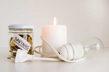 Candle with burning flame, next to unlit bulb. Energy saving and rationing. Increase in tariffs and energy crisis.
