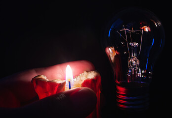 Burning candle near a switched off light bulb in complete darkness. Blackout, load shedding,...
