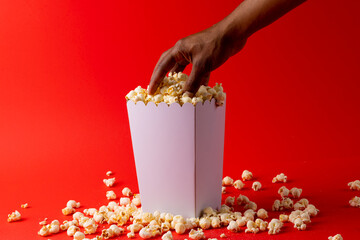 Image of hand of african american man taking away pop corn from box on red surface