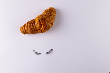 Image of croissant and fake eyelashes lying on white background