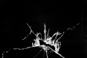 Close up of broken, cracked pane of glass with central hole, on black background with copy space