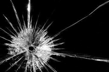 Close up of broken, cracked pane of glass with bullet hole, on black background with copy space