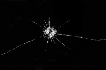 Image of broken, cracked pane of glass with central bullet hole, on black background