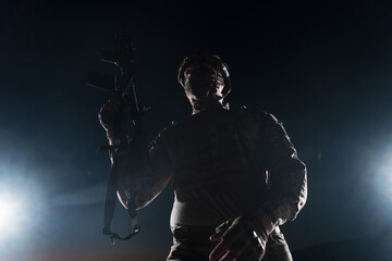 Army soldier in Combat Uniforms with an assault rifle, plate carrier and combat helmet going on a dangerous mission on a rainy night. 