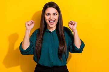 Photo of charming lucky woman wear green shirt rising fists smiling isolated yellow color background