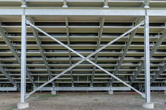 Straight On View Of Under Stadium Bleachers, Steal I-Beam Bleachers With X Cross Brace, With Stone Surface.	Nondescript Location With No People In Image.  Not A Ticketed Event.