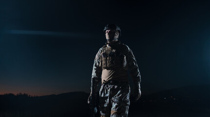 Army soldier in Combat Uniforms with an assault rifle, plate carrier and combat helmet going on a dangerous mission on a rainy night. 