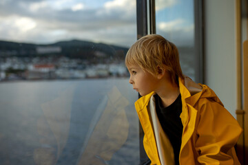 Child toddler boy on a ferry on a fjord, sunset on the deck of ferry on sunny day