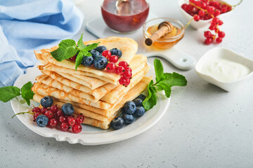 Pancakes. Stack of crepes or thin pancakes with berries, blueberries, red currants, raspberries and honey for breakfast. Homemade breakfast. Copy space. Selective focus.