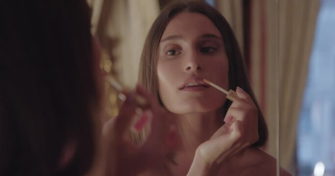 Young woman applying lipgloss near mirror