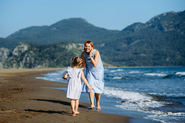 Cute little toddler girl and mother in blue dresses runnig and playing with waves on the wild beach. Turkey, Iztuzu beach,  Dalyan. Mom and daughter