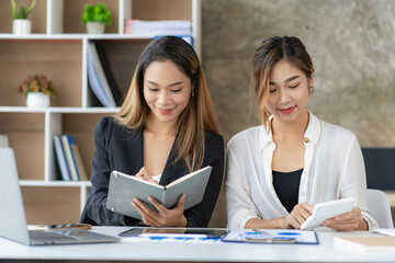 A team of Asian businesswomen discussing something and smiling as they sit at a desk in the office of women working together analyzing finances.