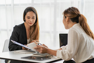 A team of Asian businesswomen discussing something and smiling as they sit at a desk in the office of women working together analyzing finances.