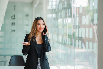 Fototapeta premium Successful businesswoman talking on her phone next to a glass wall in the office.