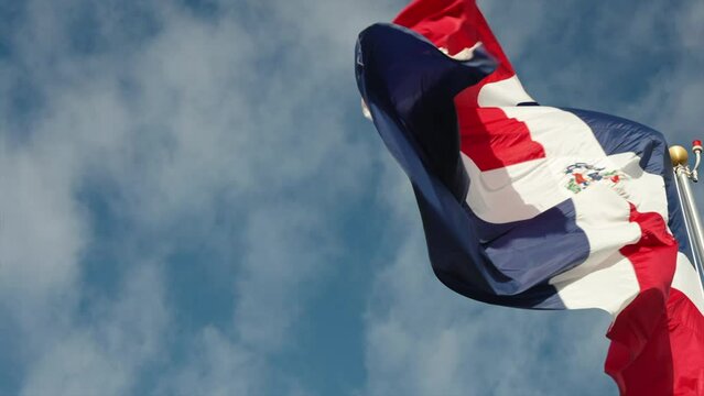 Dominican Republic national flag waving in the wind against blue sky with white clouds