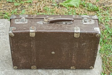 a large old handmade retro suitcase in a dark color with iron latches stands on a concrete surface in the street during the 