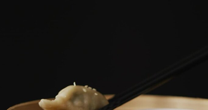 Chopsticks with gyoza dumpling in bamboo steamer on black background