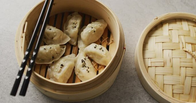 Composition of bamboo steamer with gyoza dumplings and chopsticks on grey background
