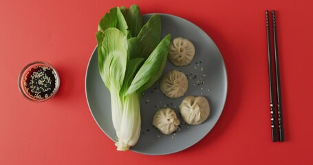 Composition of plate with dim sum dumplings, pak choi and chopsticks on red background